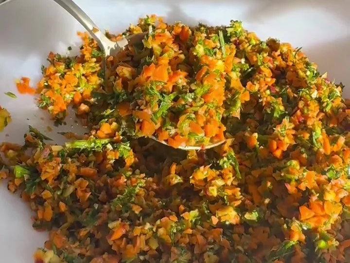 Finely chopped carrot and carrot leaf salad in a white bowl