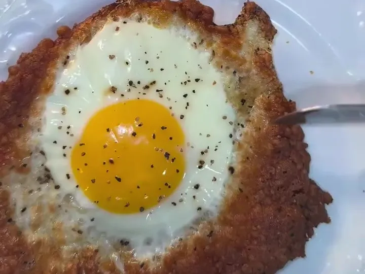A baked egg in a crisp Parmesan ring on a white plate