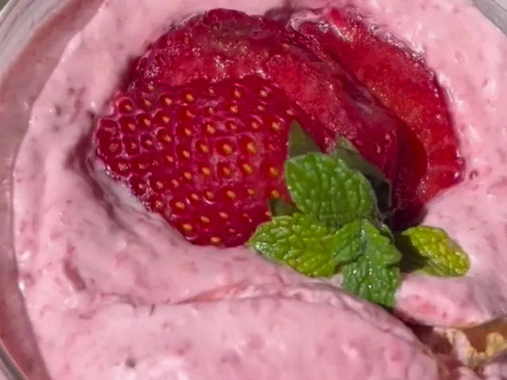 Pink strawberry mousse in a glass topped with a sliced strawberry and mint
