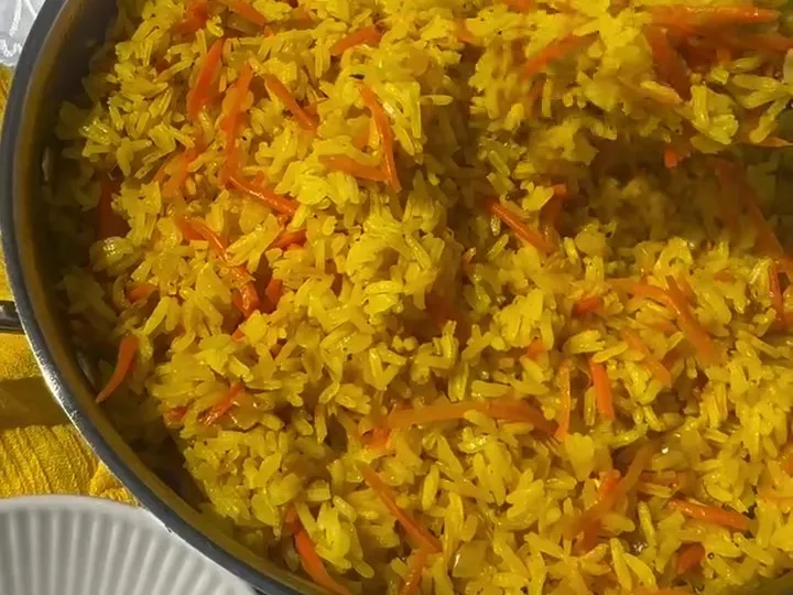 Yellow turmeric rice with shredded carrots in a pan