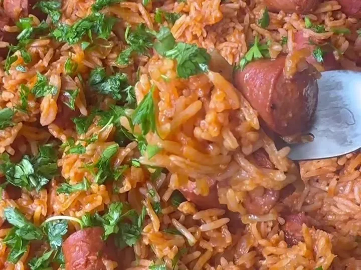 Tomato rice with sliced hotdogs and chopped parsley in a skillet
