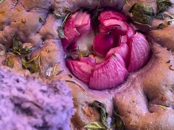 Baked ube focaccia with a purple onion rose in the center and a torn piece showing the purple crumb