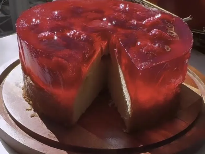 Sponge cake topped with a layer of red gelatin and raspberries, with a slice cut out