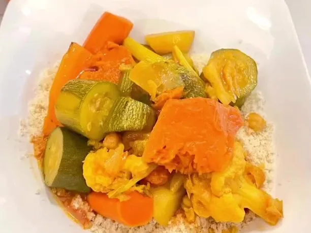 Cooked vegetables served over couscous on a white plate